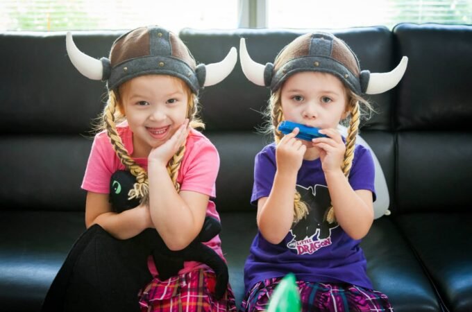 Two children wearing Viking-style horned helmets are posing on a black leather couch.