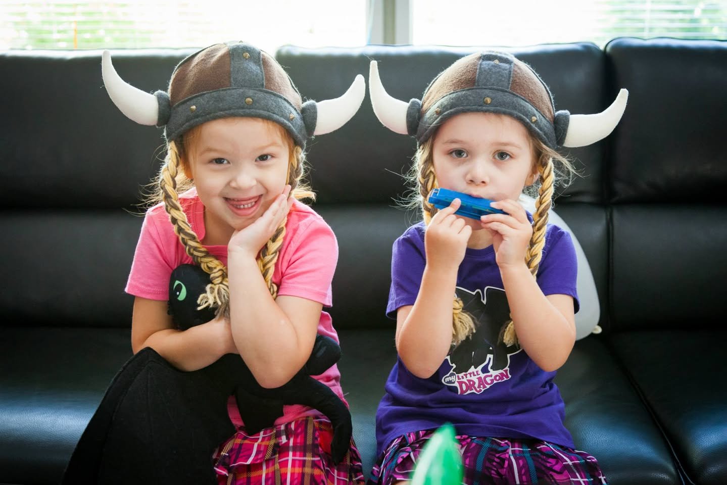 Two children wearing Viking-style horned helmets are posing on a black leather couch.