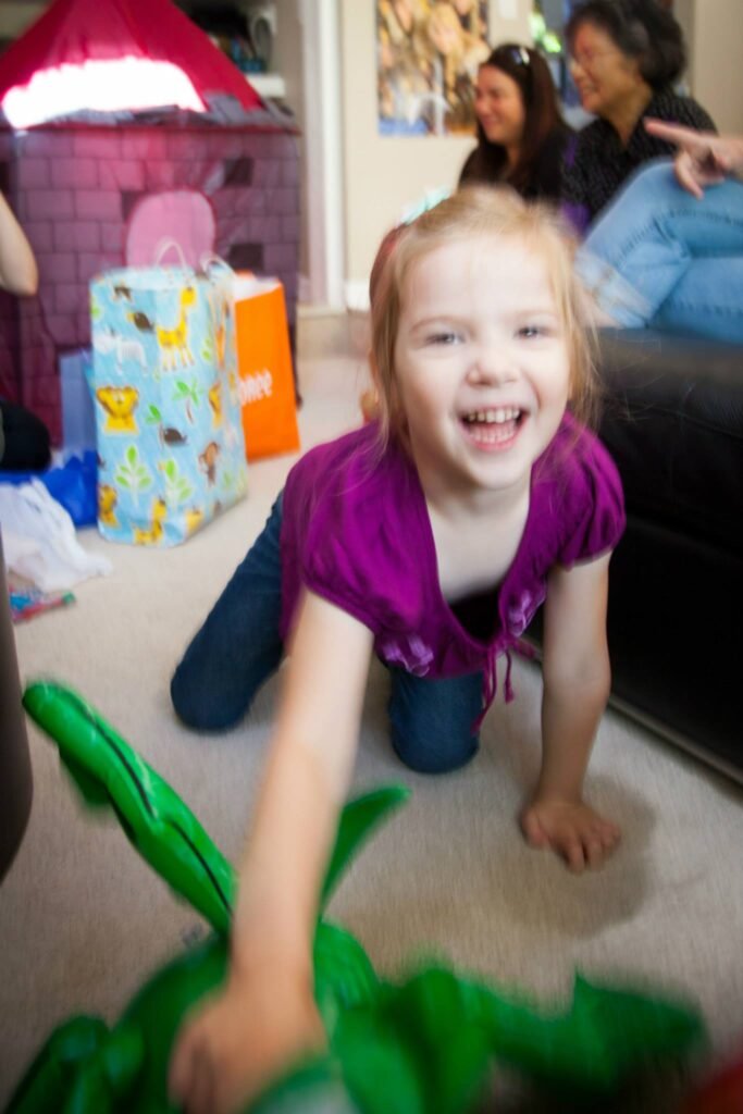 A smiling child reaches for a green toy elephant during a family gathering in the Pacific Northwest.