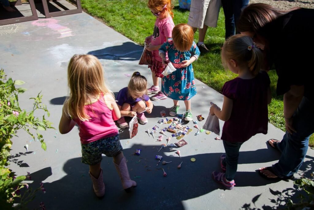 A group of children engagement in outdoor play, likely collecting water beads, and an adult overseeing the activity on a sunny day.