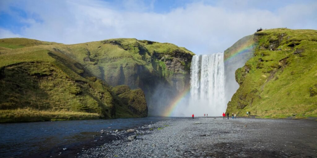 Stunning view of Skogafoss waterfall in Iceland with a breathtaking rainbow and lush green hills.
