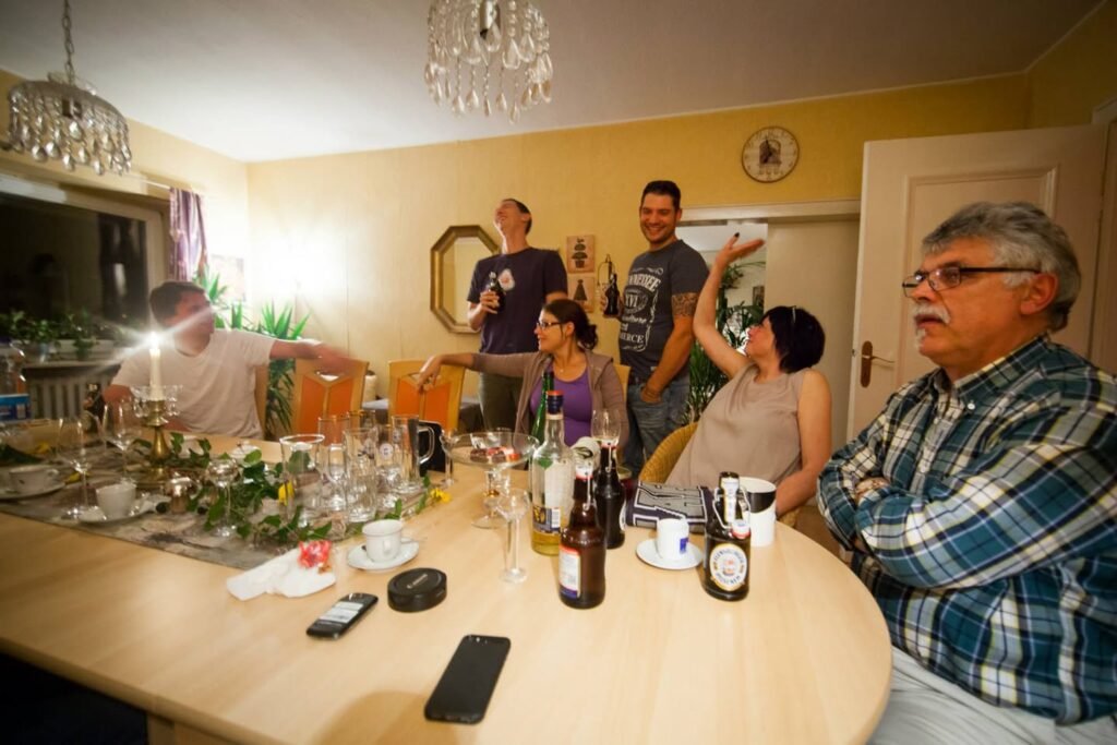Friends enjoying a casual wine tasting around a dining table set with bottles and glasses. The cozy home features warm yellow walls and festive decorations.