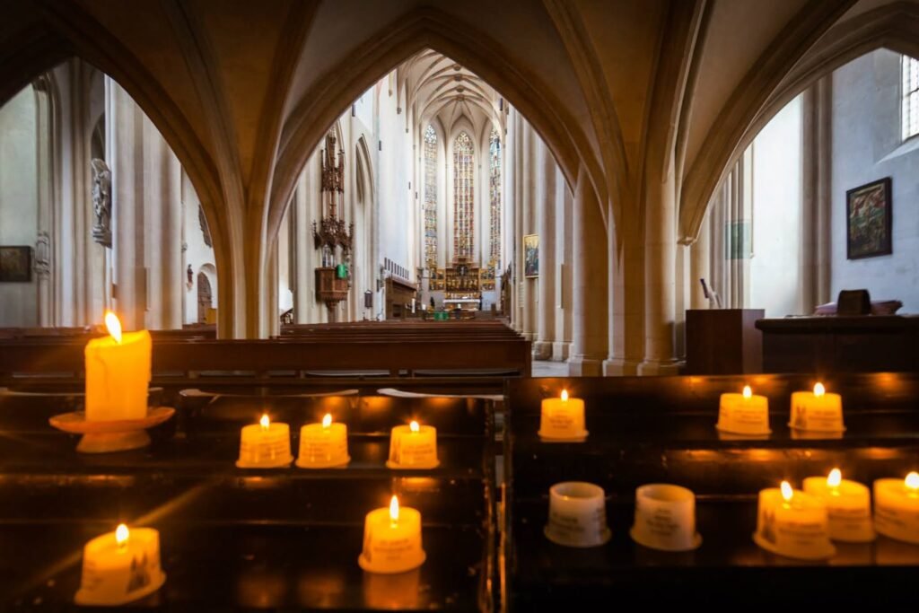 Rows of burning votive candles near Gothic arches illuminate a traditional church interior.