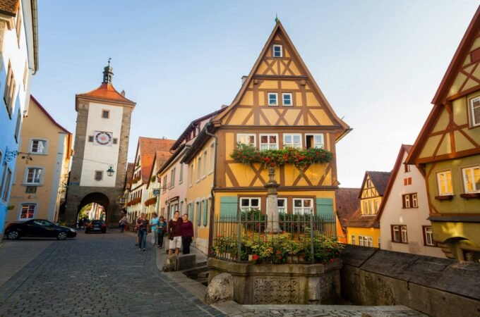 A picturesque European town featuring traditional half-timbered houses with steep roofs and a historic clock tower in the background.
