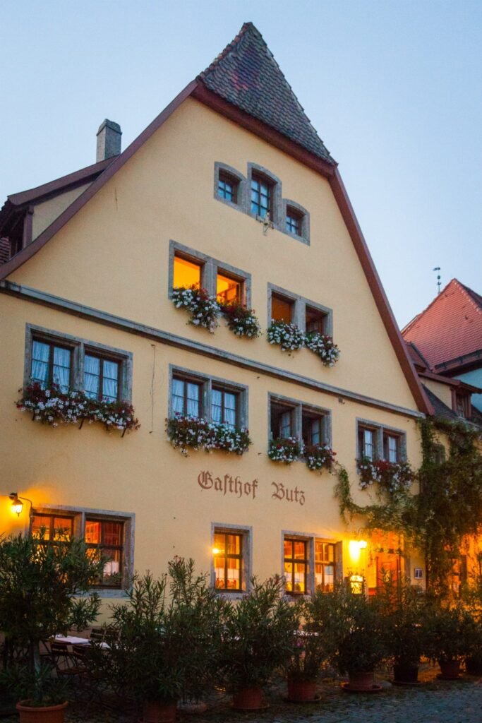 A yellow European-style building with flower boxes and warm window lights at evening.