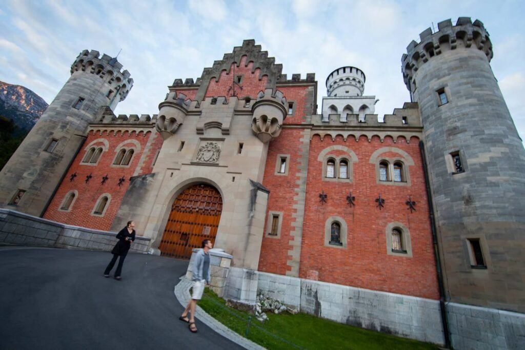 Detailed views of a historic red brick castle featuring stone towers and mountain background.