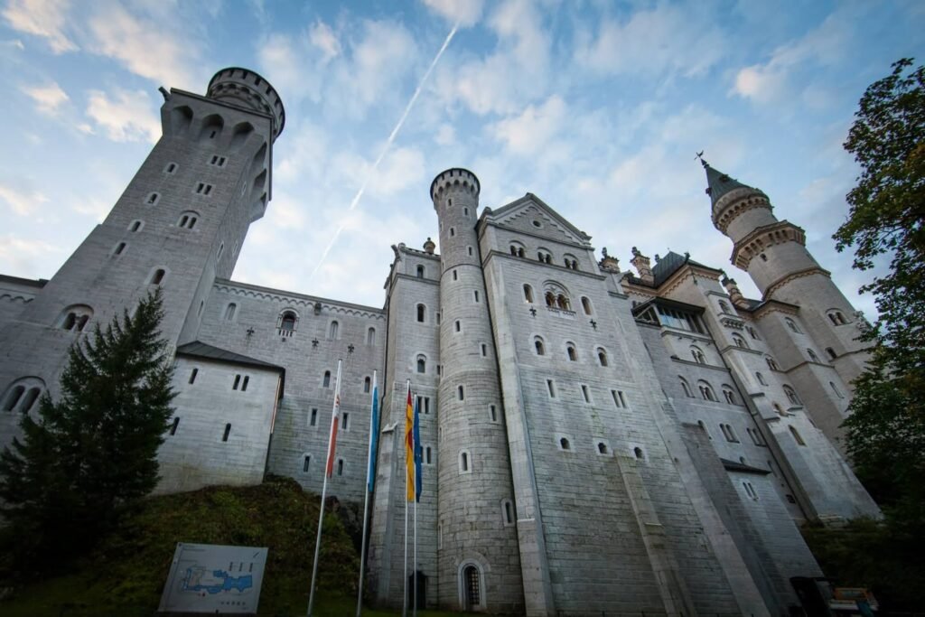 A panoramic view of a large stone castle with multiple towers under a cloudy sky