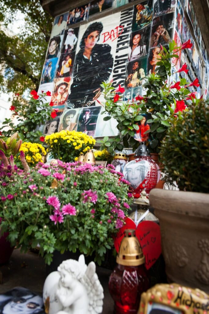 A vibrant display of pink and red flowers alongside fan art and photos at a public memorial.