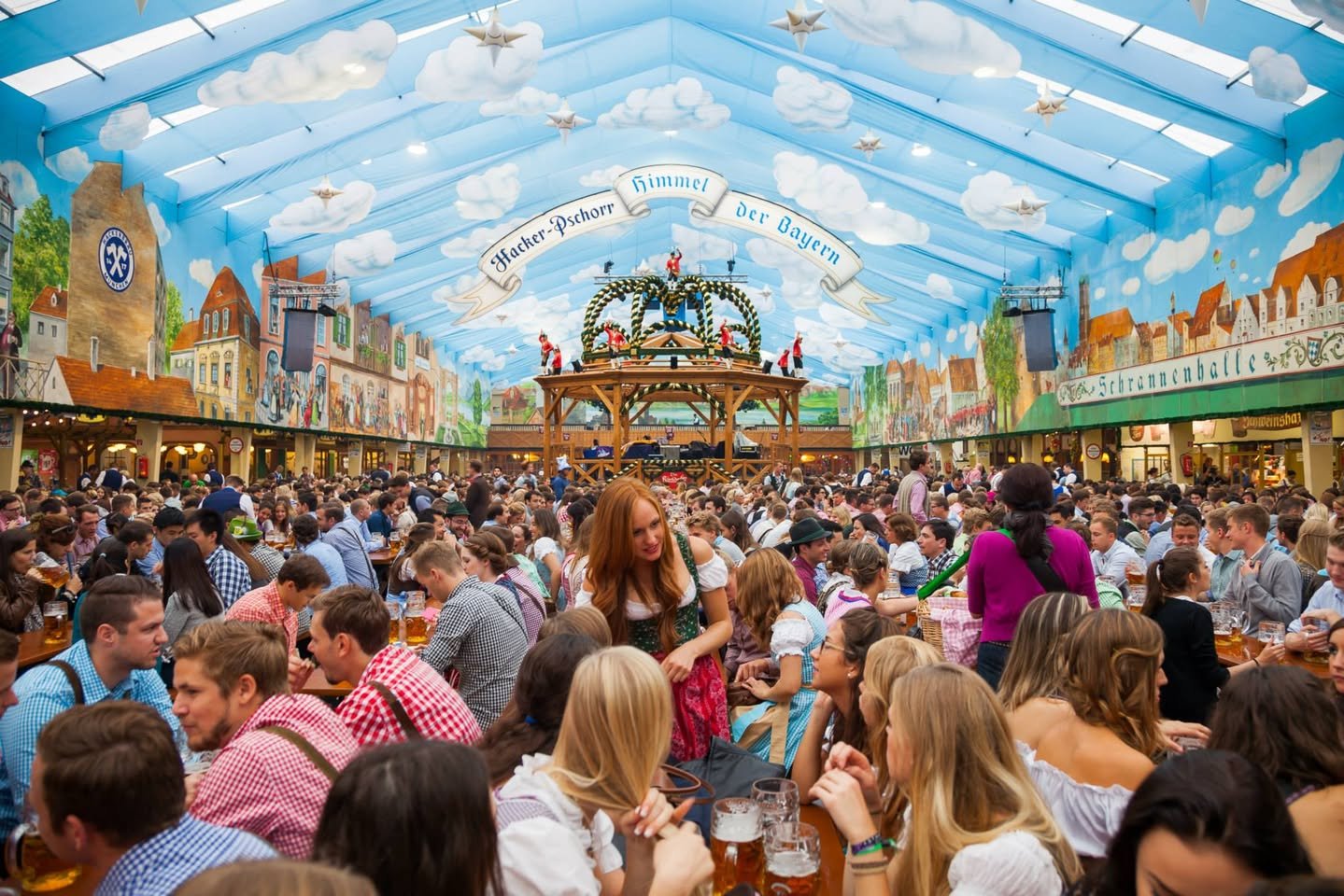 Oktoberfest Busy beer hall crowded with guests under a vibrant painted ceiling mural.