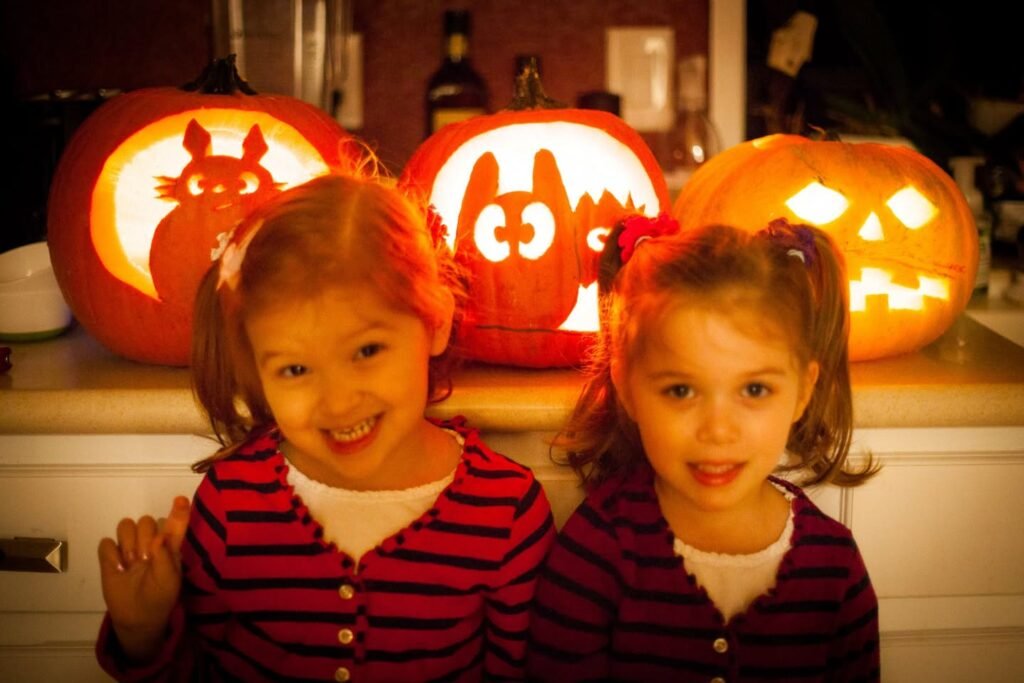 Two children posing in front of creatively carved pumpkins featuring the LotR and Frodo. The pumpkin designs are illuminated from within.