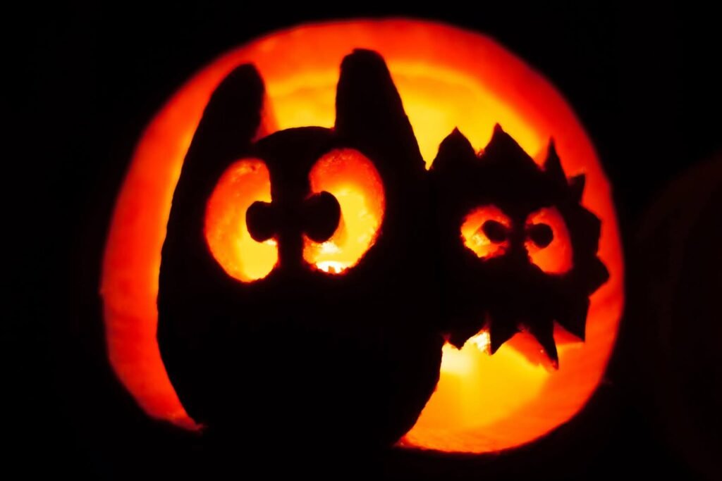 A glowing Halloween pumpkin featuring a silhouette design of a large owl with a baby on its back. The carved faces are illuminated by warm interior light.