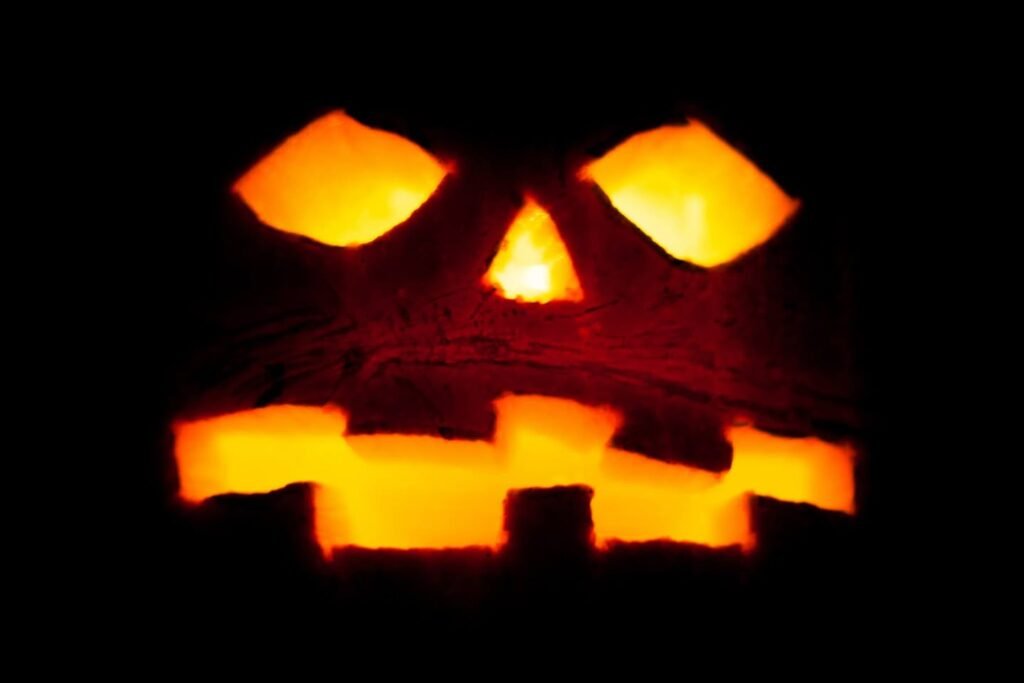 A spooky carved jack-o'-lantern glowing in the dark with a classic grin. The orange light casts an eerie and festive Halloween atmosphere.