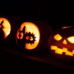 Oktoberfest A row of illuminated jack o lanterns carving unique faces that include a cat, a spider, and a classic pumpkin.