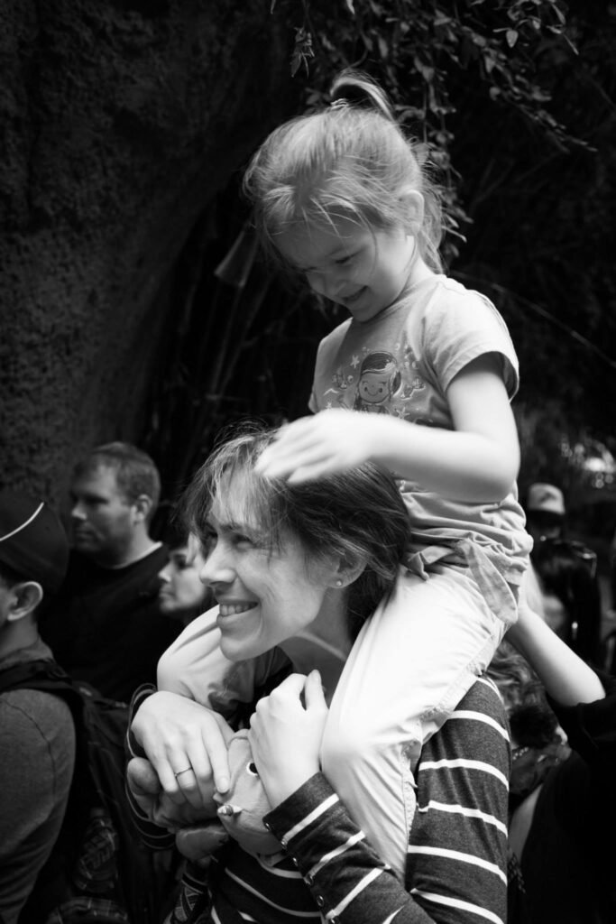 A smiling mother carries a young child on her shoulders in a black and white photo.