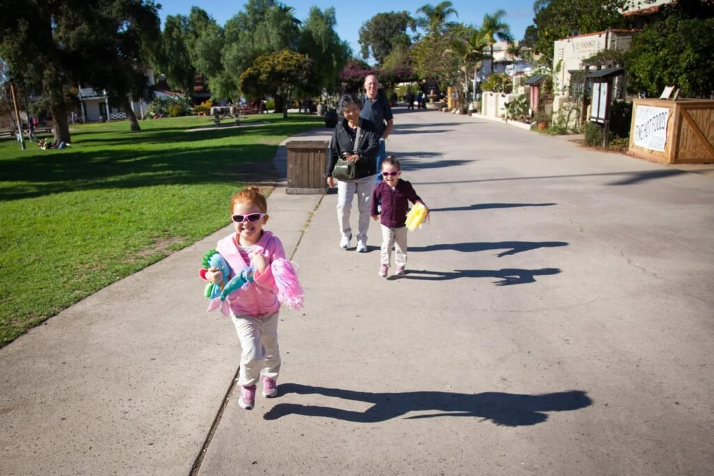 A family walks together on a wide paved path in a sunny park.