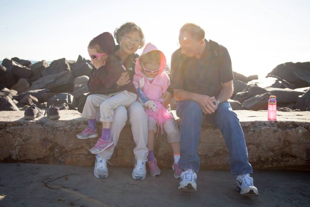 Two adults and two children sitting on rocks near water on a sunny day.