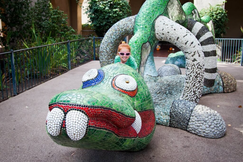 A child poses with a large green mosaic dragon sculpture featuring white teeth and a long wrapped body.