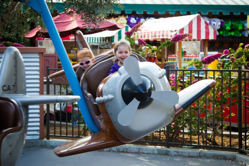 A vibrant playground scene with happy kids on a swinging airplane ride, set against colorful umbrellas and festive market stalls.