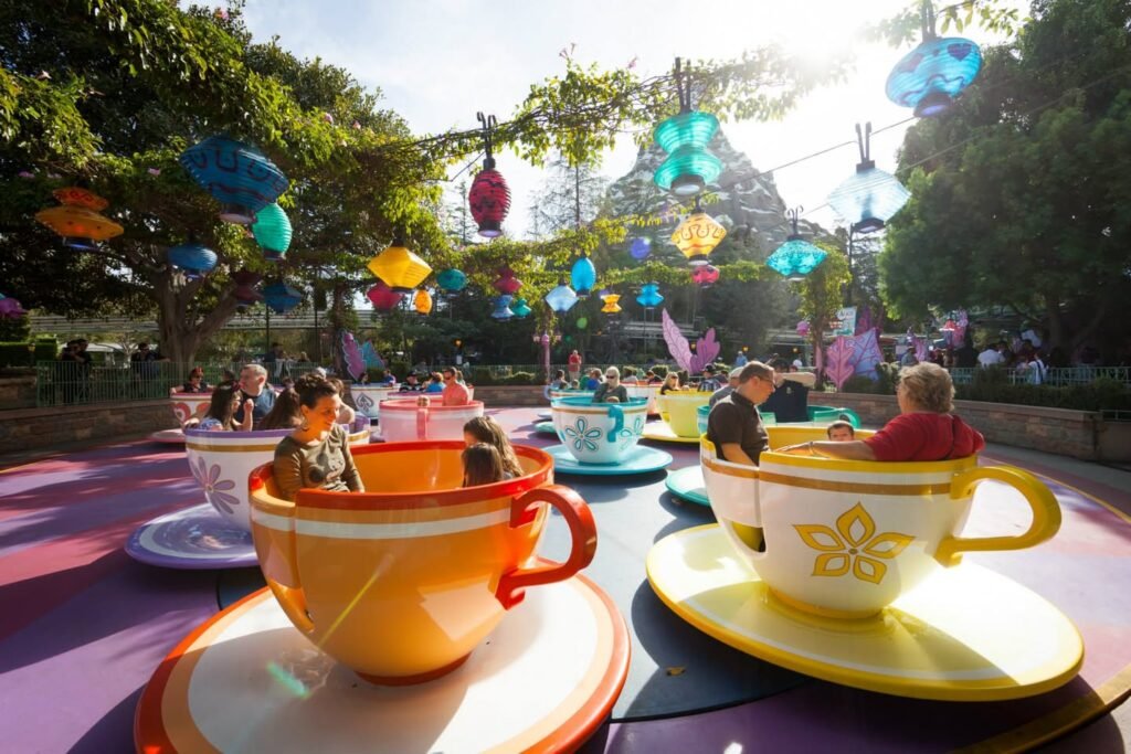 Vibrant teacup attraction with passengers enjoying the ride amidst colorful hanging ornaments and lush greenery.