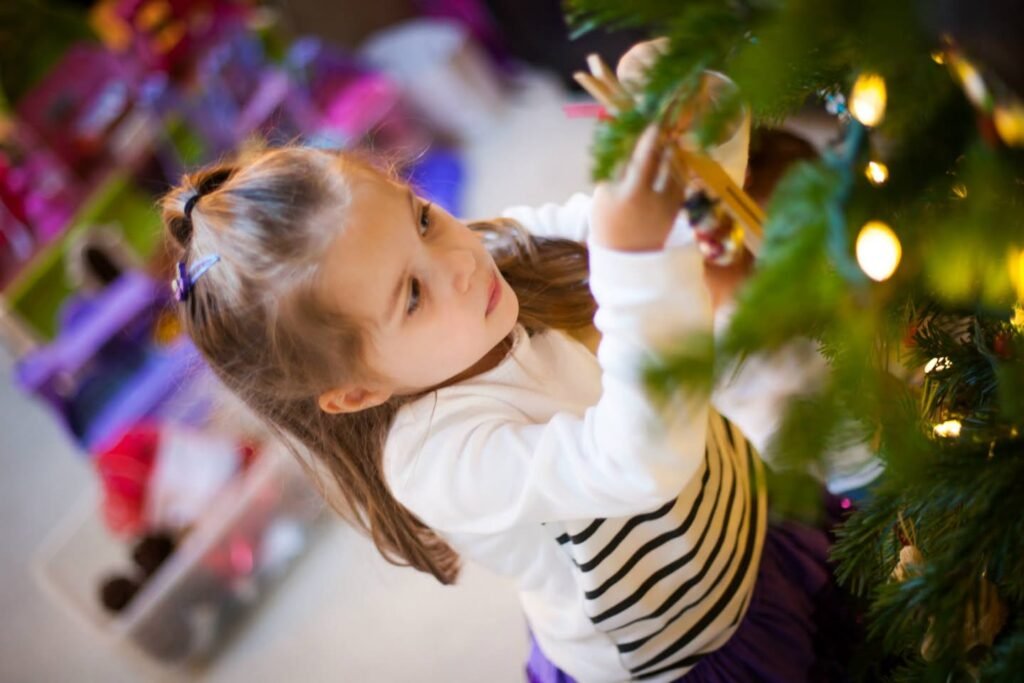 A child reaches for the tips of a Christmas tree branch while holding a golden star ornament.