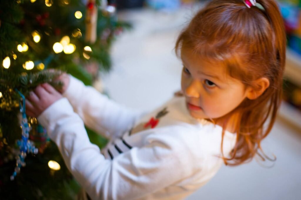 A young child carefully decorating a Christmas tree. Close-up details of hands placing ornaments on the tree branches.
