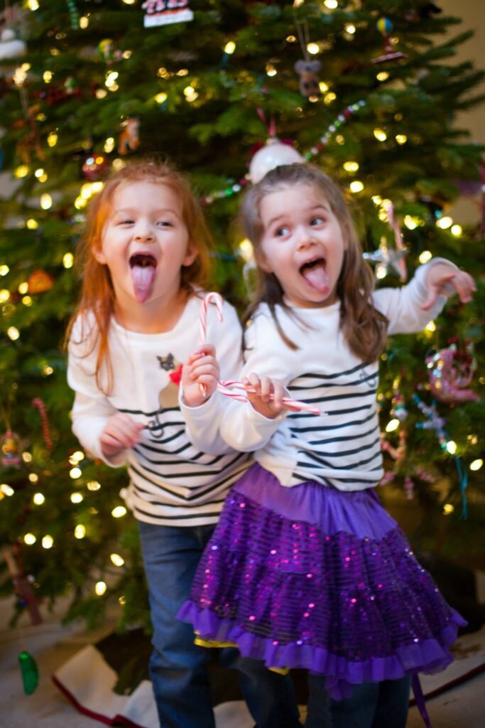 Children playfullypose in front of a decorated Christmas tree, holdingcandies and wearingfestiveclothes.