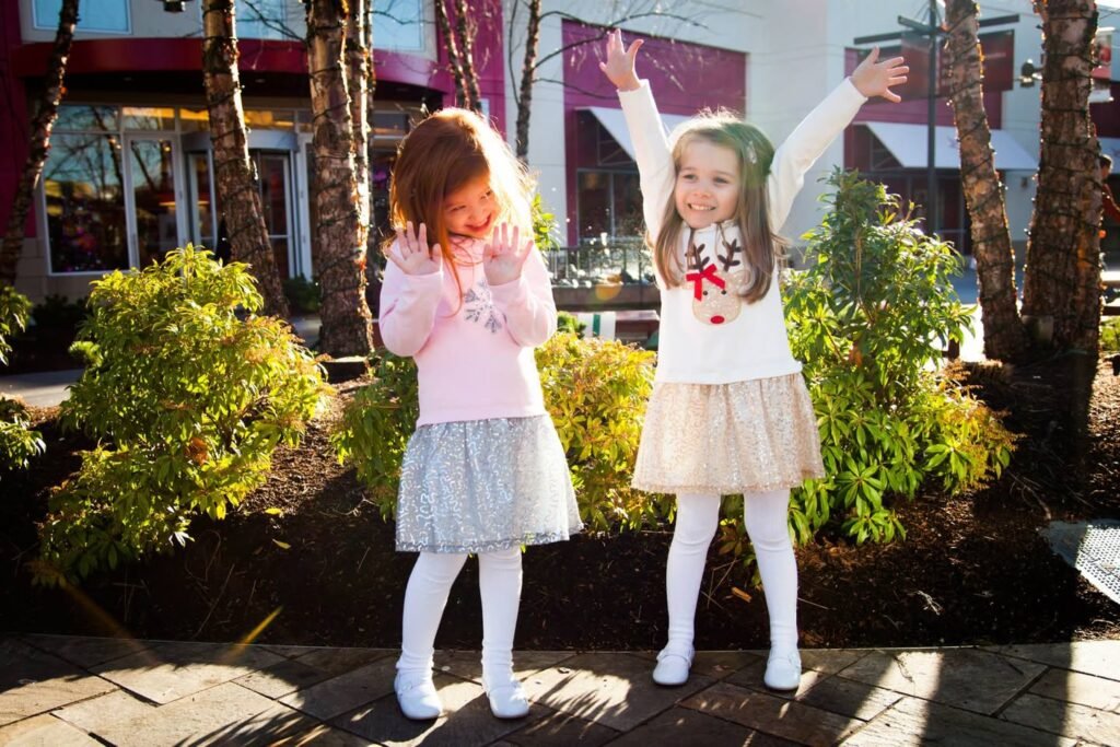 Two young children playing joyfully on a sunlit paved patio surrounded by trees.