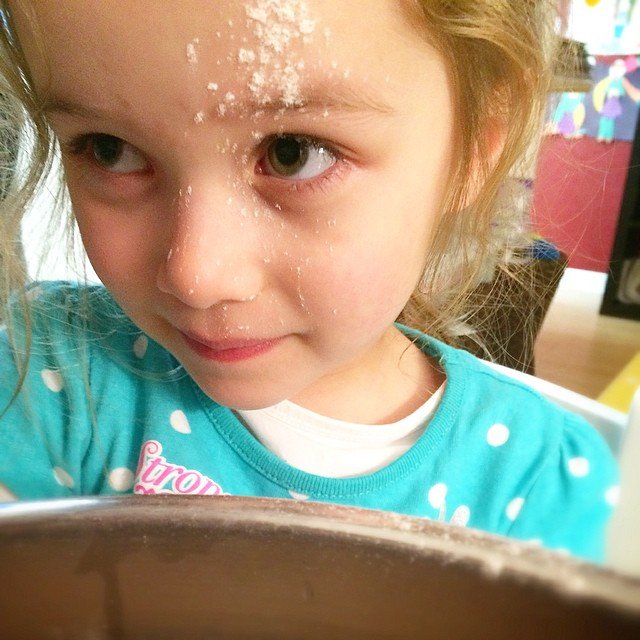 A child with flour on their forehead looks over a mixing bowl during baking.