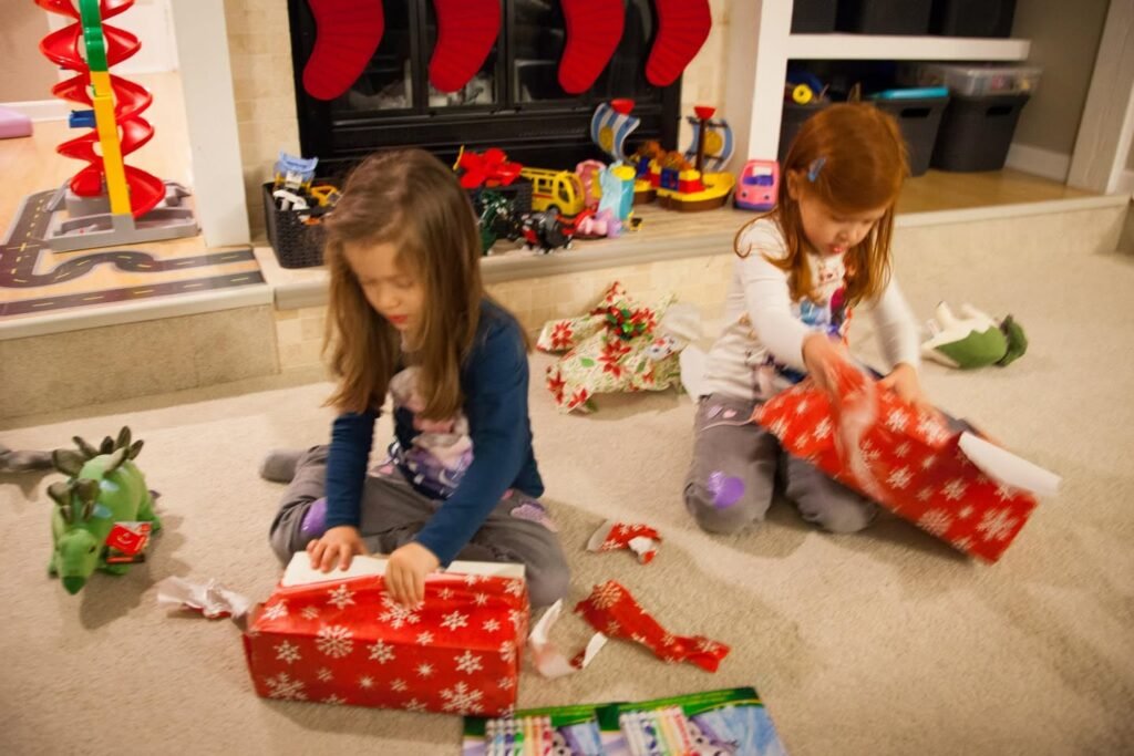 Children opening Christmas presents near a decorated fireplace with red stockings.