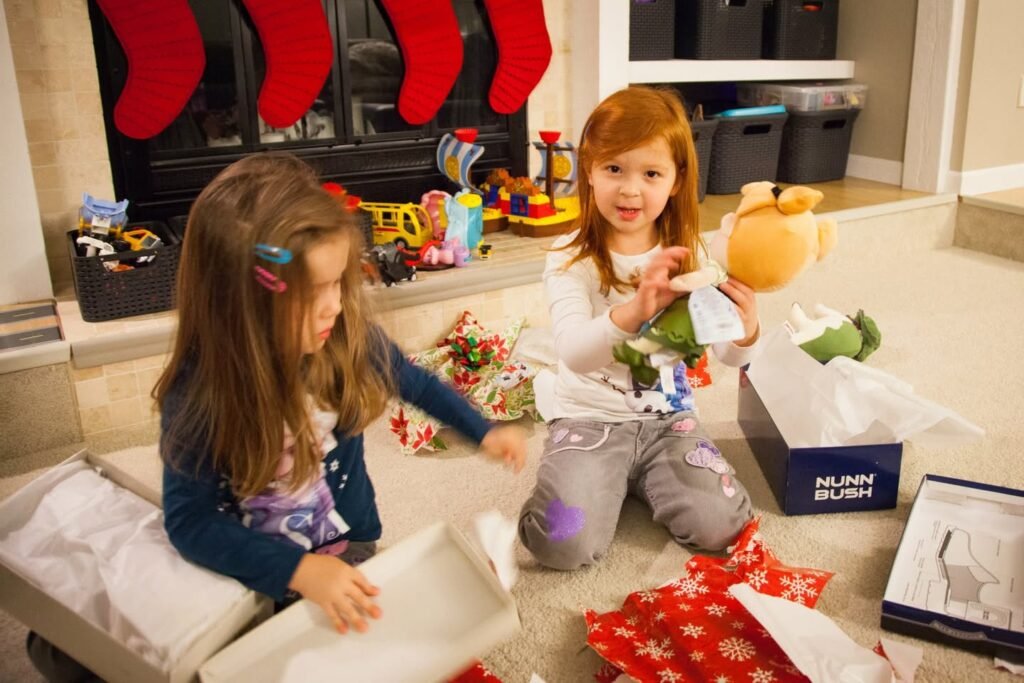 Children opening Christmas presents in a cozy living room with red stockings hanging on the fireplace.