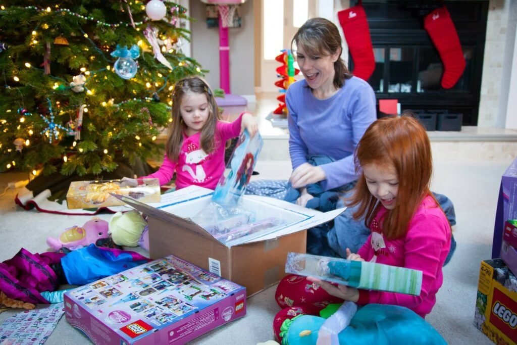 Family members enjoying gift opening on Christmas morning near a decorated tree and fireplace with stockings.