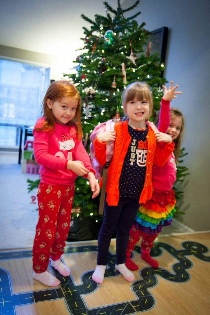 Children in colorful pajamas pose together next to a decorated Christmas tree with lights and ornaments.