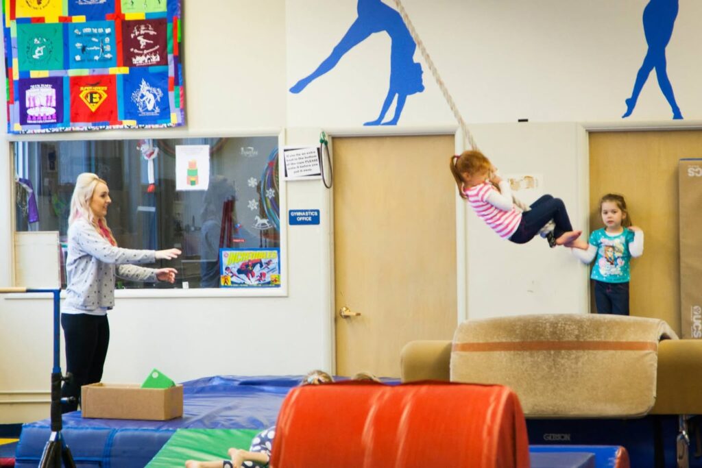 Children exercised on a trapeze in a vibrant gym with colorful mats and equipment.