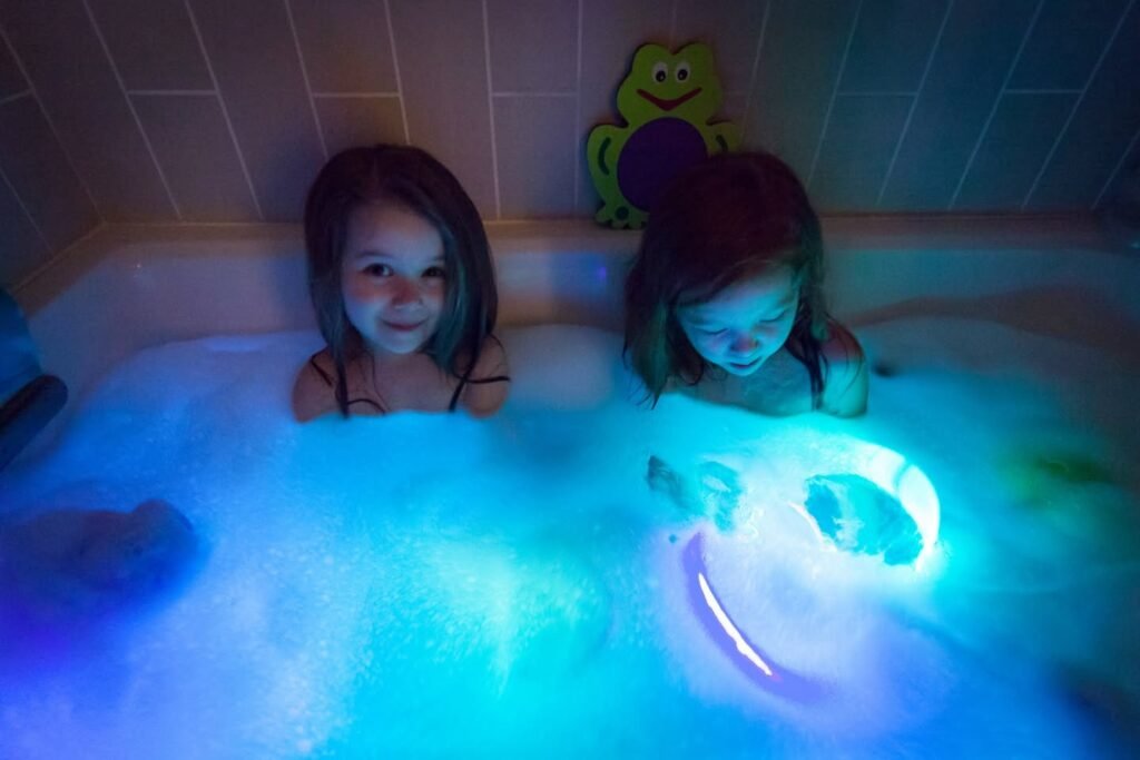 Two children enjoy a bubble bath illuminated by blue glow light.