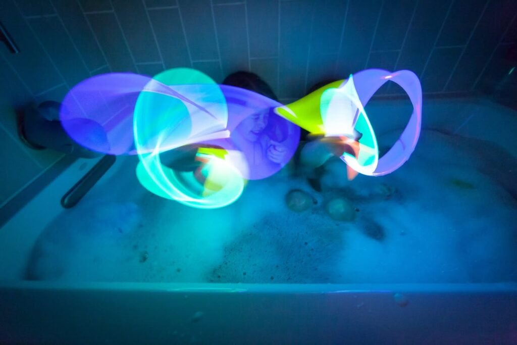 Long-exposure light painting with glowing blue, purple, and green trails. Vibrant abstract shapes formed against a dark, tiled background.