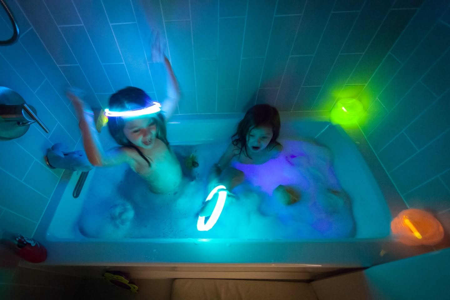 Bath Rave Children playing with bright glow sticks and toys in a dark bathroom tub.
