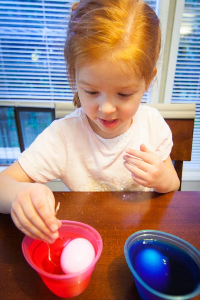 A child carefully dyeing Easter eggs in plastic cups at a table.