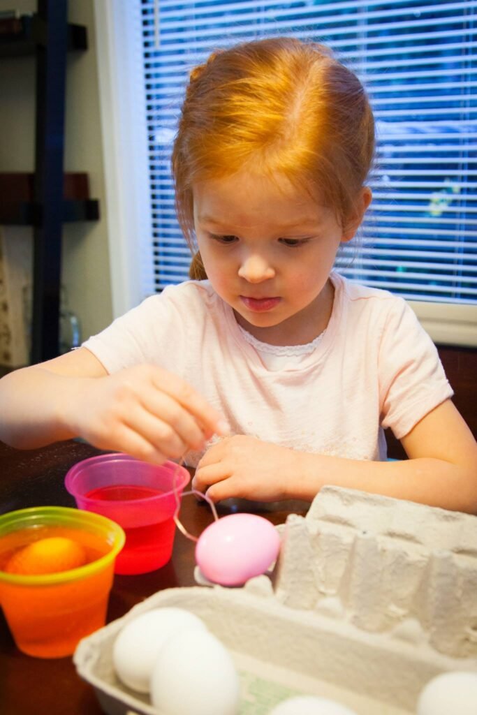 A child carefully dyes an Easter egg using bright dyes at the kitchen table.