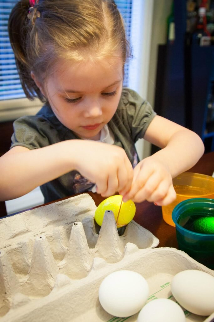 A young child decorates eggs at the table with an egg carton nearby