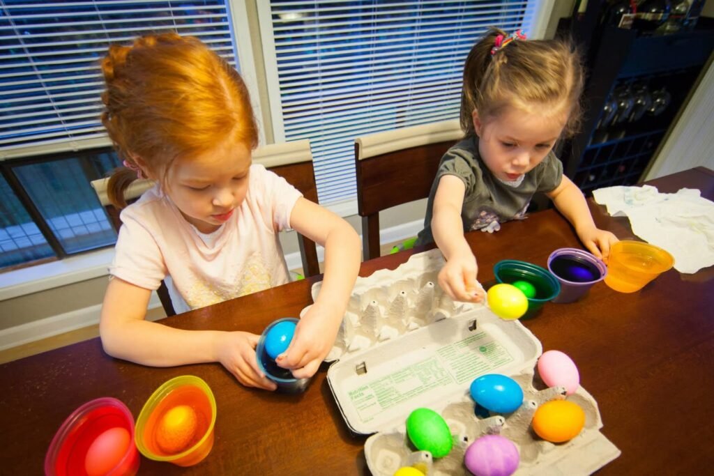 Children carefully painting eggs in an egg carton at a dining table.