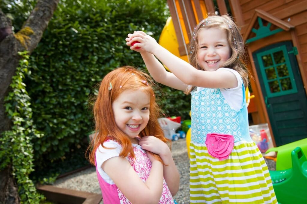 Two children enjoying time at a backyard playhouse with colorful dresses and greenery in the background.