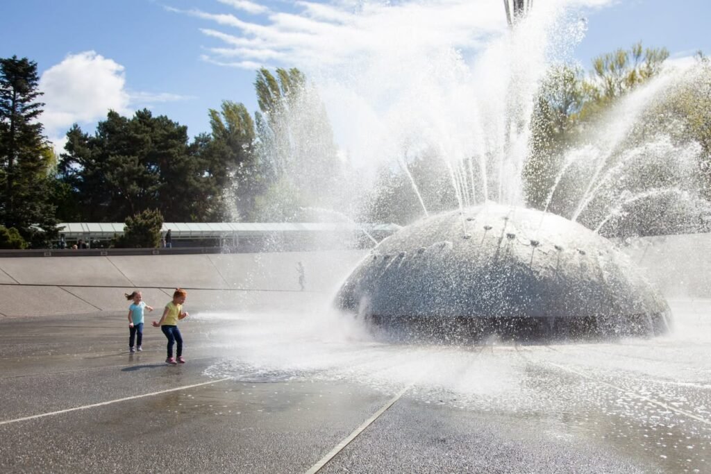 Water spraying high into the air from a large garden fountain against a blue sky.