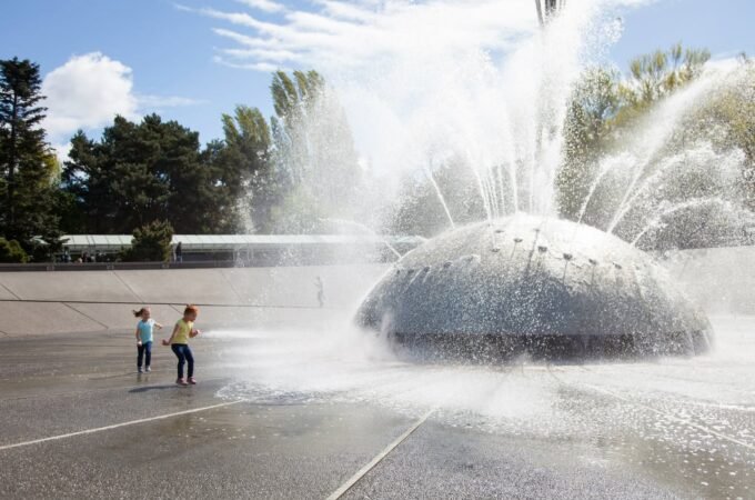 Water spraying high into the air from a large garden fountain against a blue sky.