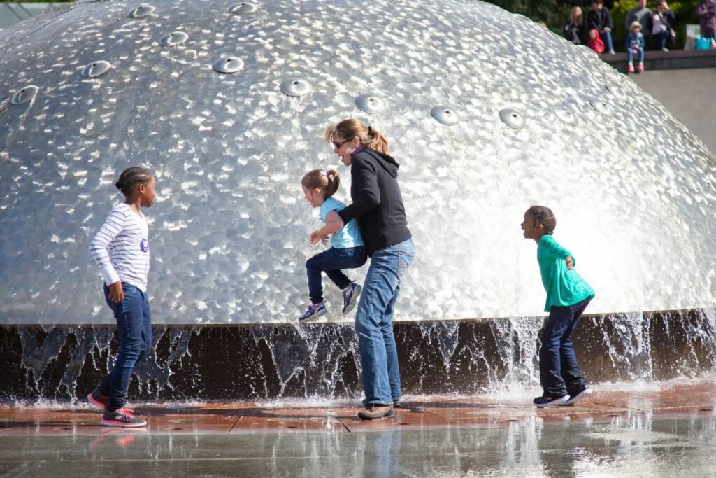 Children and adults enjoy playing around a large dome fountain with cascading water.