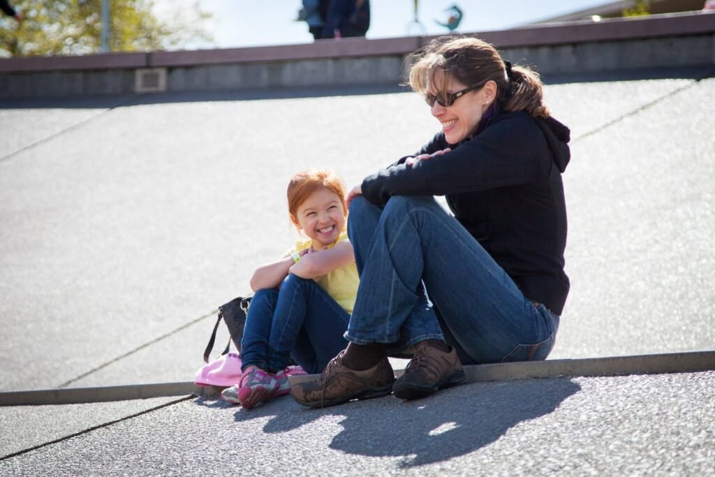 Two individuals sitting together outdoors in a bright, open environment with a low concrete wall in the background.