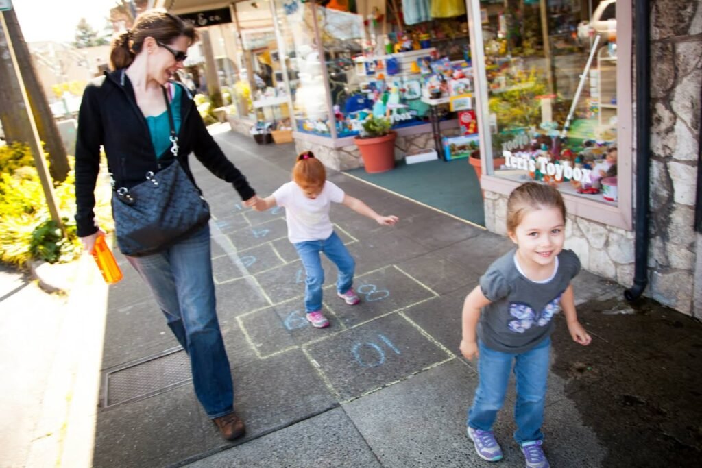 An adult and two children enjoying a sunny day on a sidewalk with a toy store display in the background.