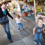An adult and two children enjoying a sunny day on a sidewalk with a toy store display in the background.