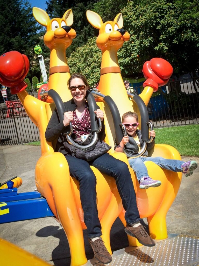 Two people riding a boxing kangaroo amusement park ride. Close-up shots highlight the vibrant yellow kangaroo head and red boxing glove.