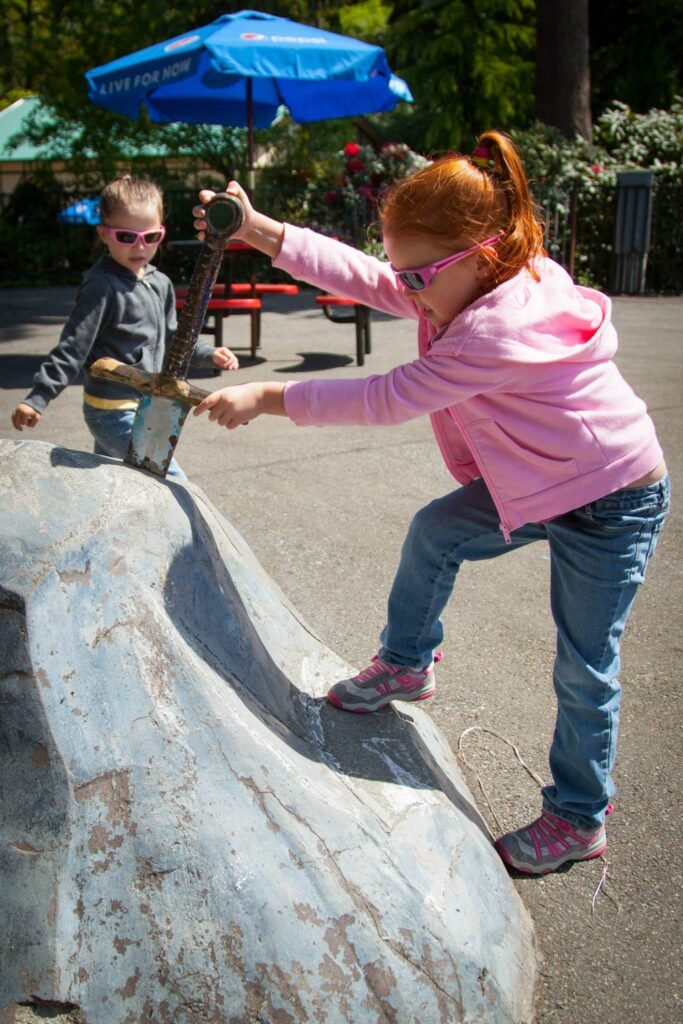 Two kids climbing on a large stone in a sunny park