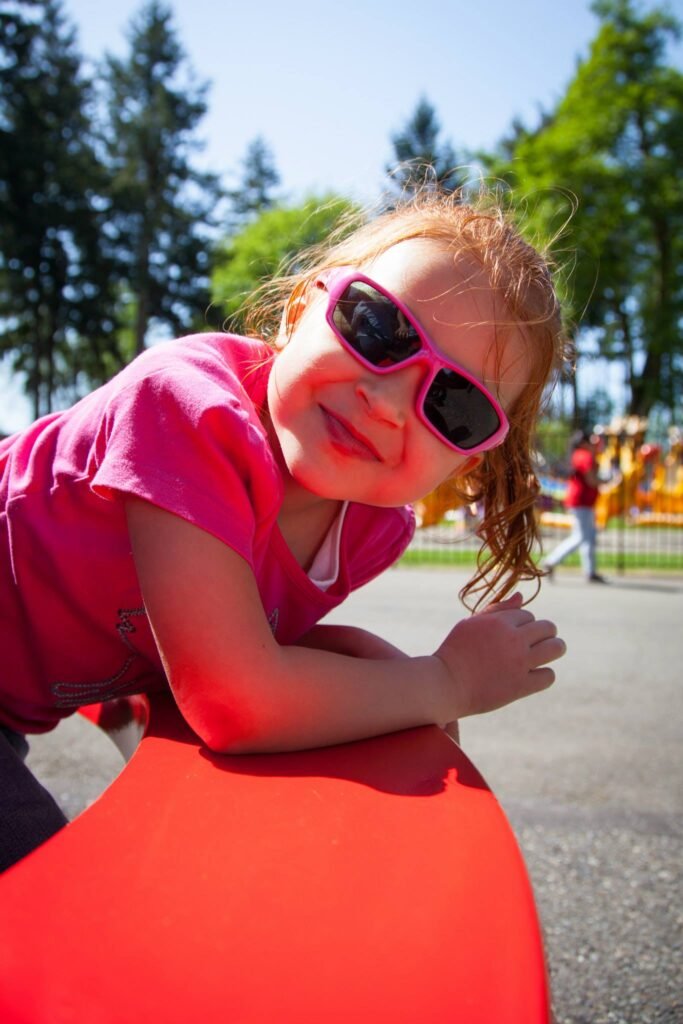 A child wearing pink sunglasses smiles brightly outdoors.